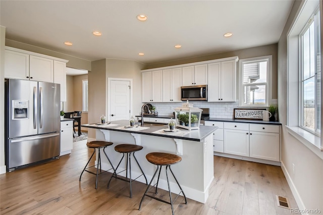 kitchen featuring appliances with stainless steel finishes, dark countertops, visible vents, and tasteful backsplash