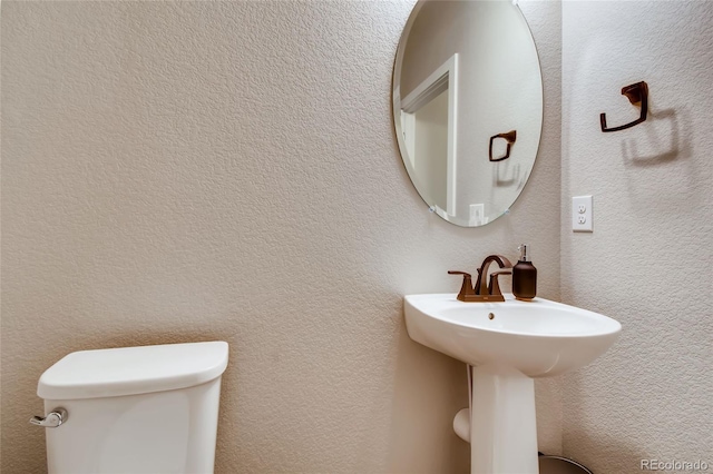 half bathroom featuring toilet, a sink, and a textured wall