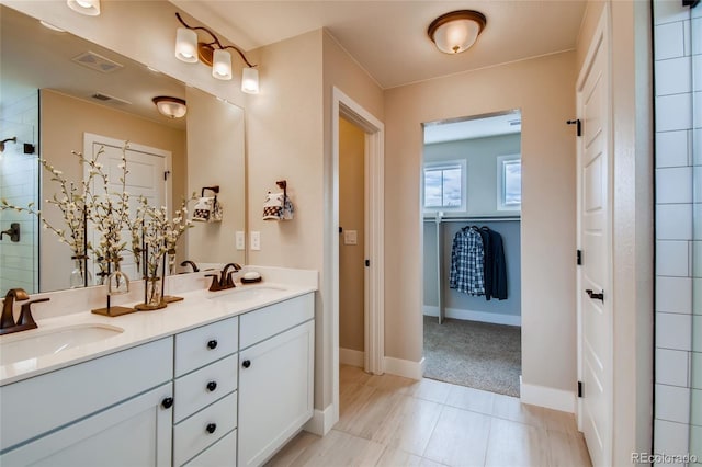 bathroom featuring tiled shower, a sink, visible vents, and double vanity