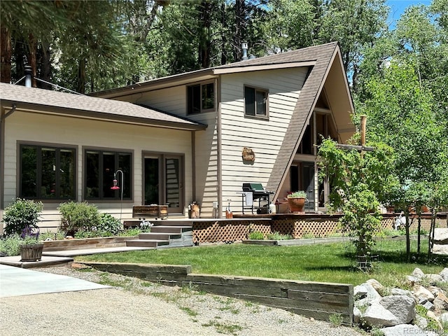 rear view of property featuring a lawn and a shingled roof