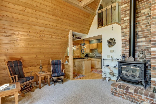 living room with wooden walls, ceiling fan, light carpet, a wood stove, and high vaulted ceiling