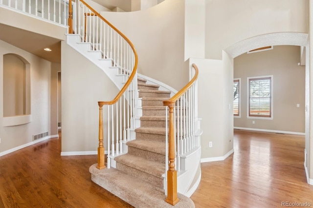 stairway with arched walkways, a high ceiling, and wood finished floors
