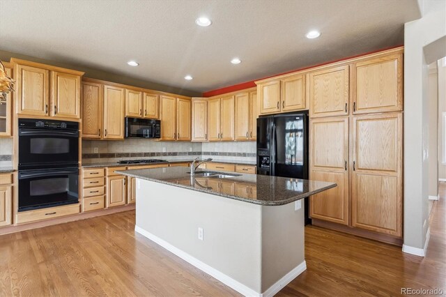 kitchen featuring a sink, dark stone countertops, black appliances, recessed lighting, and light wood-style floors