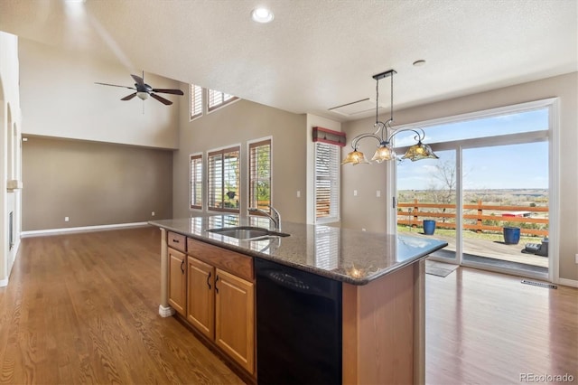kitchen with wood finished floors, a ceiling fan, dark stone countertops, a sink, and dishwasher