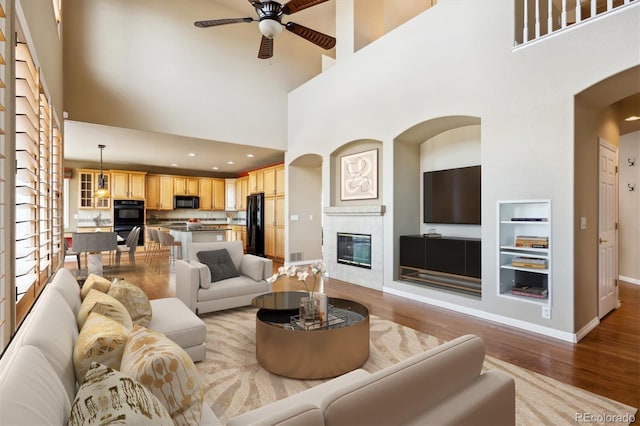 living room featuring wood finished floors, a towering ceiling, ceiling fan, and arched walkways