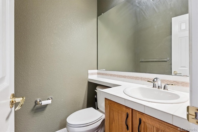 bathroom with toilet, vanity, and a textured wall