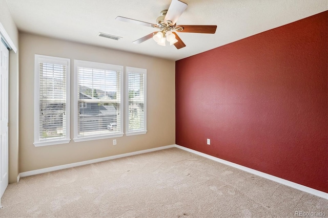 carpeted spare room with visible vents, baseboards, ceiling fan, and a textured wall