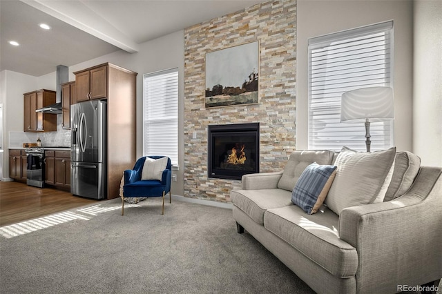 living room with baseboards, beamed ceiling, dark carpet, a stone fireplace, and recessed lighting