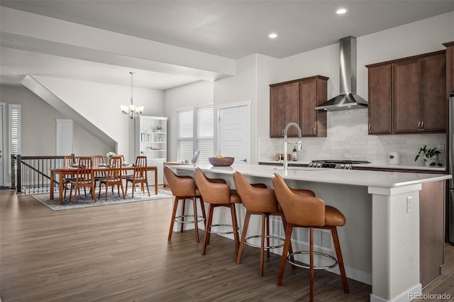 kitchen featuring tasteful backsplash, wall chimney range hood, light countertops, wood finished floors, and a sink