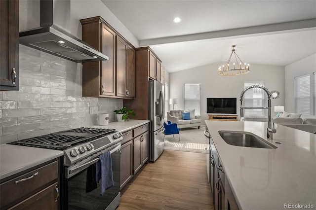 kitchen featuring a sink, appliances with stainless steel finishes, open floor plan, and wall chimney range hood