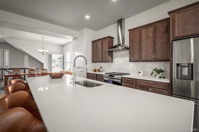 kitchen featuring backsplash, wall chimney range hood, light countertops, appliances with stainless steel finishes, and a sink