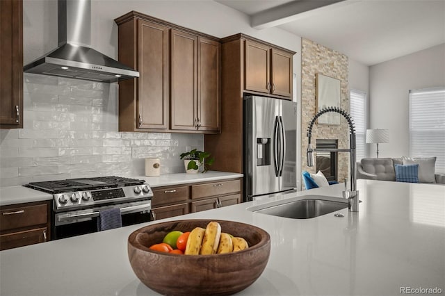 kitchen with a sink, tasteful backsplash, appliances with stainless steel finishes, and wall chimney range hood