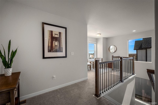 hall with an upstairs landing, visible vents, carpet floors, and baseboards