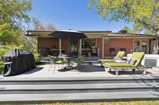 rear view of property with brick siding, a wooden deck, and outdoor dining space