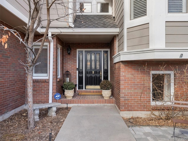 view of exterior entry featuring brick siding and a shingled roof