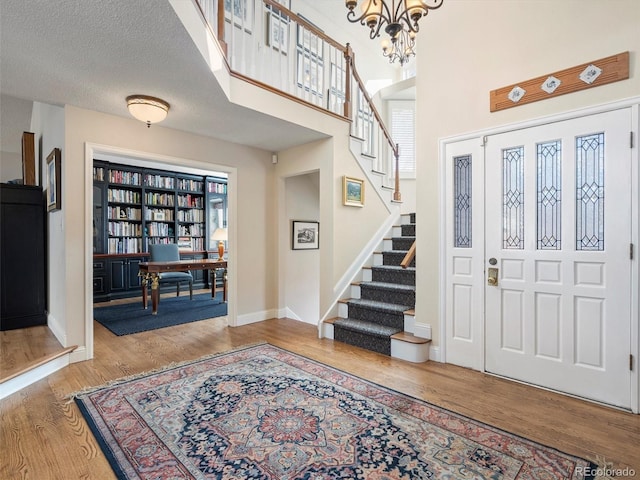 entrance foyer with baseboards, wood finished floors, stairs, a textured ceiling, and a notable chandelier