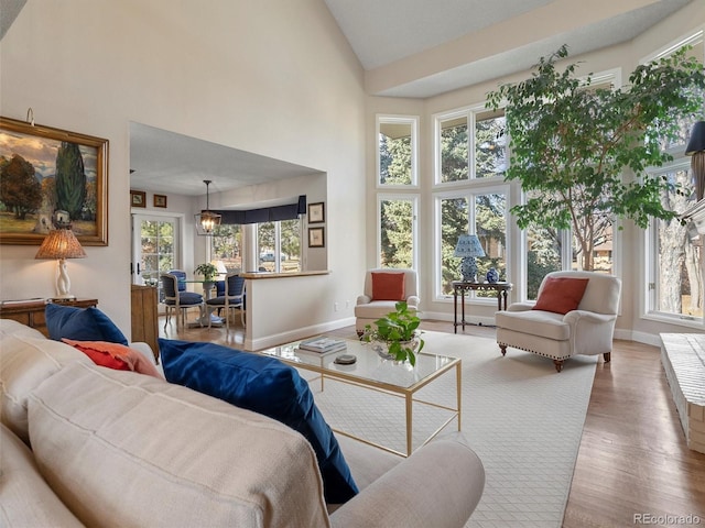 living room with high vaulted ceiling, an inviting chandelier, wood finished floors, and baseboards