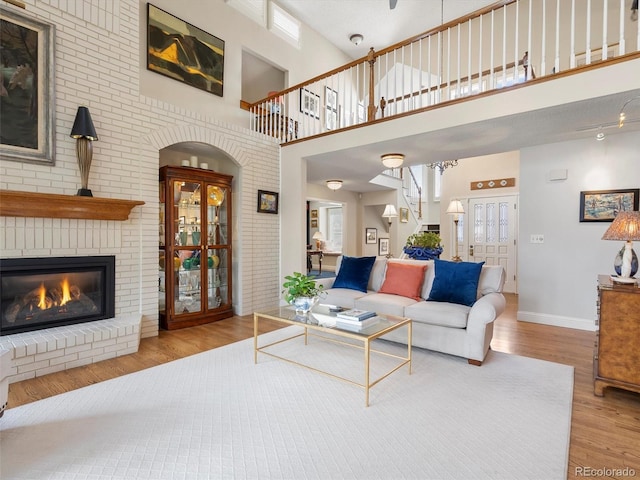 living room featuring light wood-type flooring, a brick fireplace, a towering ceiling, and baseboards