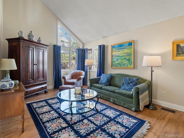 living room with visible vents, light wood-style floors, vaulted ceiling, a textured ceiling, and baseboards