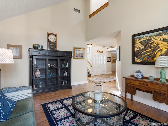 living room with dark wood-style flooring, visible vents, high vaulted ceiling, baseboards, and stairs