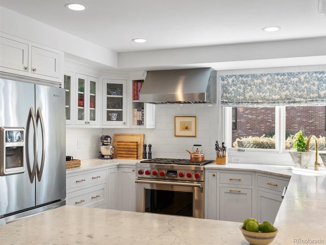 kitchen featuring tasteful backsplash, glass insert cabinets, range hood, stainless steel appliances, and white cabinetry