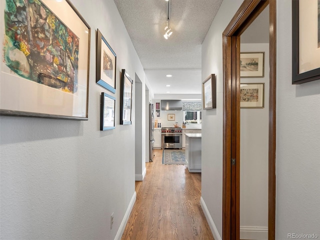 hallway featuring a textured ceiling, wood finished floors, rail lighting, and baseboards