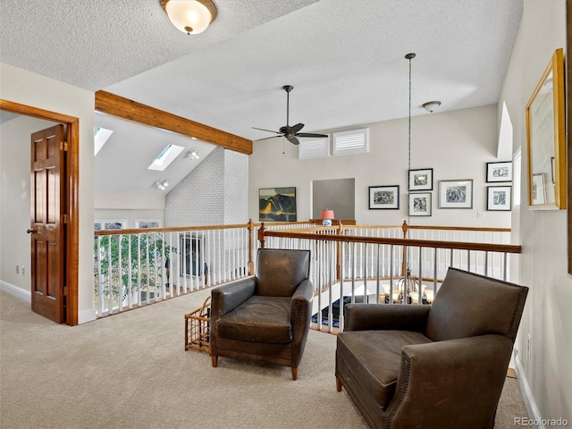 sitting room featuring a textured ceiling, vaulted ceiling with skylight, light carpet, a ceiling fan, and baseboards