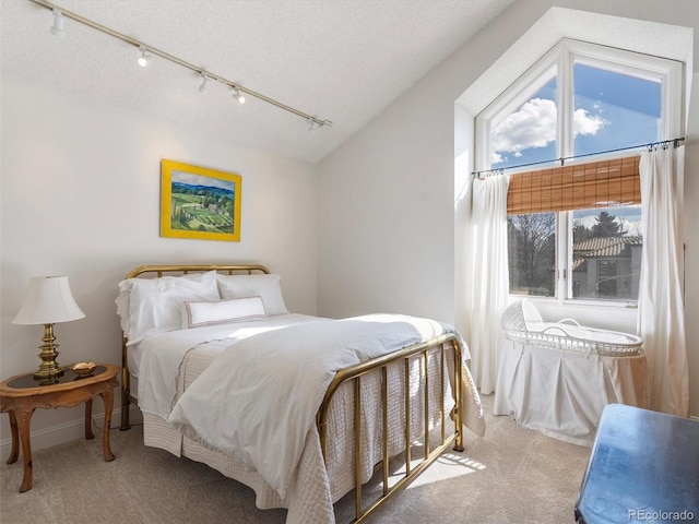 bedroom featuring light carpet, vaulted ceiling, a textured ceiling, and track lighting