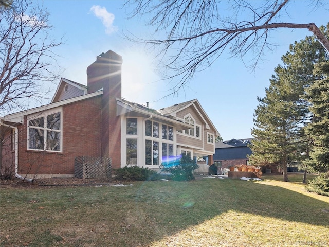 back of property featuring brick siding, a yard, and a chimney