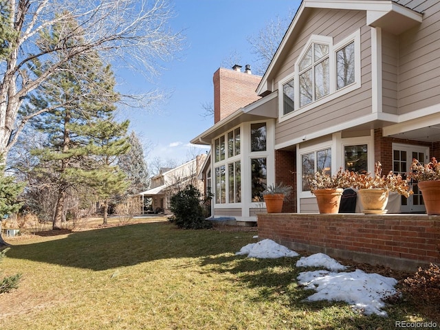 view of side of property featuring brick siding, a lawn, and a chimney