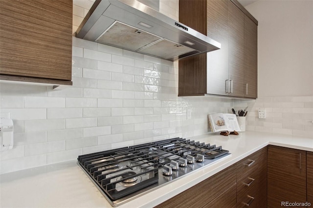 kitchen with stainless steel gas cooktop, backsplash, range hood, and light countertops
