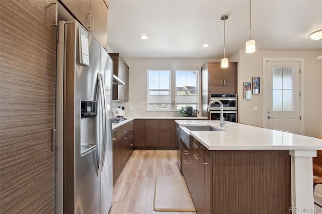 kitchen with stainless steel appliances, light wood-style flooring, modern cabinets, light countertops, and an island with sink
