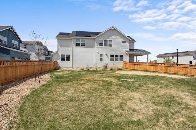 rear view of house featuring roof mounted solar panels, a fenced backyard, board and batten siding, and a yard