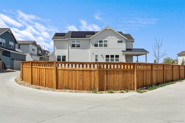 rear view of house with roof mounted solar panels, a residential view, fence private yard, and metal roof