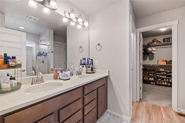 244 Chipeta Way, Lochbuie, CO 80603 - bathroom with a stall shower, double vanity, a walk in closet, wood finished floors, and baseboards