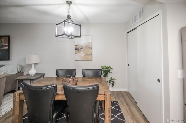 dining area with a notable chandelier, light hardwood / wood-style floors, and a textured ceiling