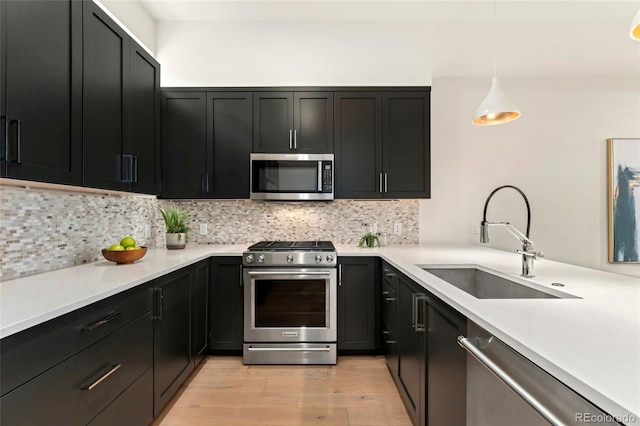 kitchen featuring sink, tasteful backsplash, hanging light fixtures, appliances with stainless steel finishes, and light hardwood / wood-style floors