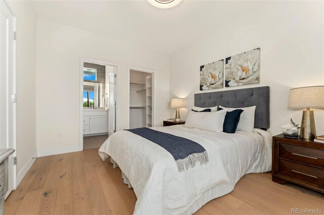 bedroom with ensuite bathroom, a spacious closet, a closet, and light hardwood / wood-style flooring