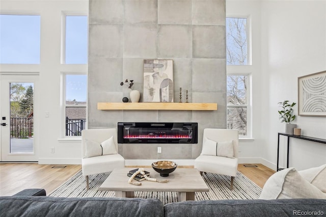 living room with a tiled fireplace, baseboards, a towering ceiling, and wood finished floors