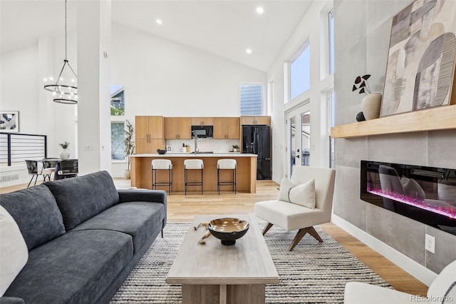 living area featuring a fireplace, high vaulted ceiling, light wood finished floors, an inviting chandelier, and a wealth of natural light