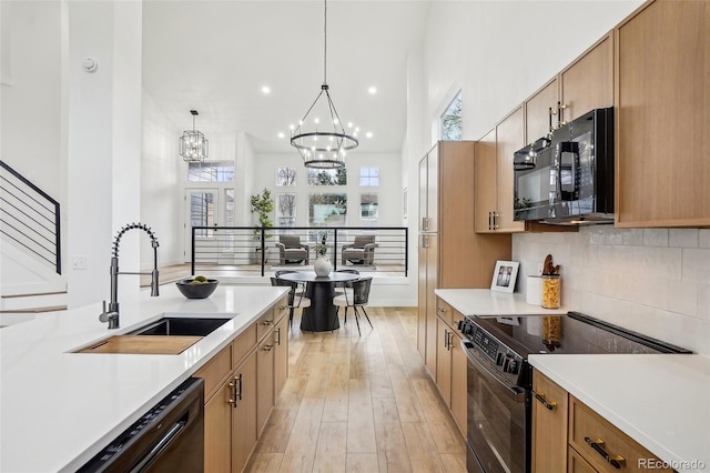 kitchen with an inviting chandelier, a sink, light countertops, decorative backsplash, and black appliances