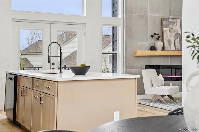 kitchen featuring a kitchen island with sink, stainless steel dishwasher, a fireplace, a sink, and light wood-style flooring