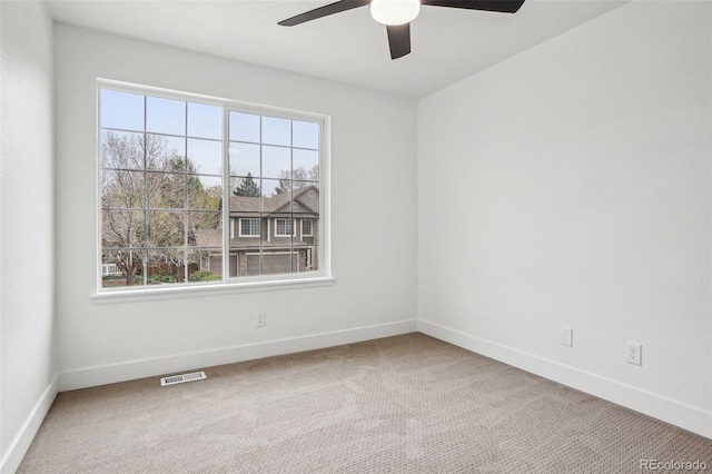 carpeted spare room featuring a healthy amount of sunlight, baseboards, a ceiling fan, and visible vents