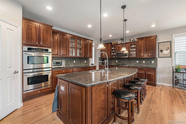10994 Shadowbrook Cir, Highlands Ranch, CO 80130 - kitchen with appliances with stainless steel finishes, light wood-type flooring, a center island with sink, decorative backsplash, and recessed lighting
