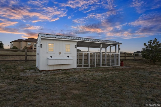 back house at dusk featuring a lawn and an outdoor structure