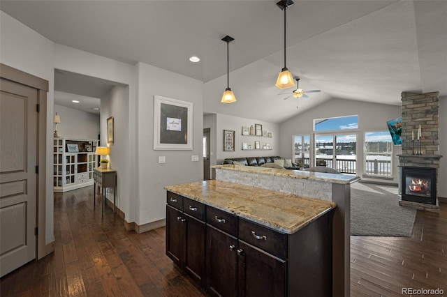 kitchen featuring ceiling fan, decorative light fixtures, a fireplace, a kitchen island, and lofted ceiling