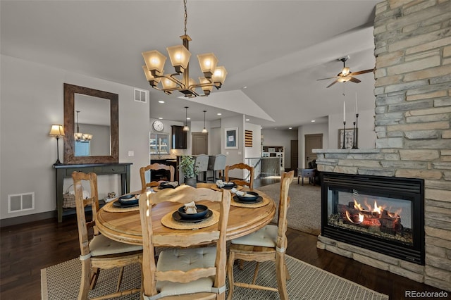 dining room with dark hardwood / wood-style floors, ceiling fan, a stone fireplace, and vaulted ceiling