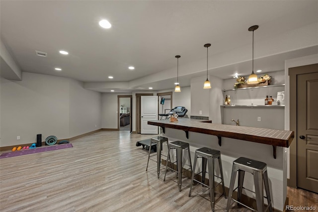 bar featuring butcher block countertops, light wood-type flooring, and hanging light fixtures