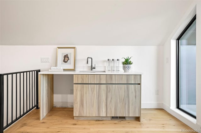 bar with sink, light brown cabinets, and light hardwood / wood-style flooring