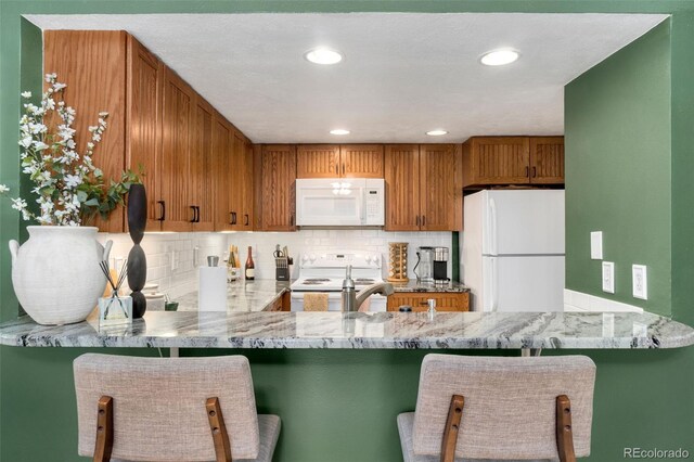 kitchen featuring a kitchen bar, white appliances, and kitchen peninsula